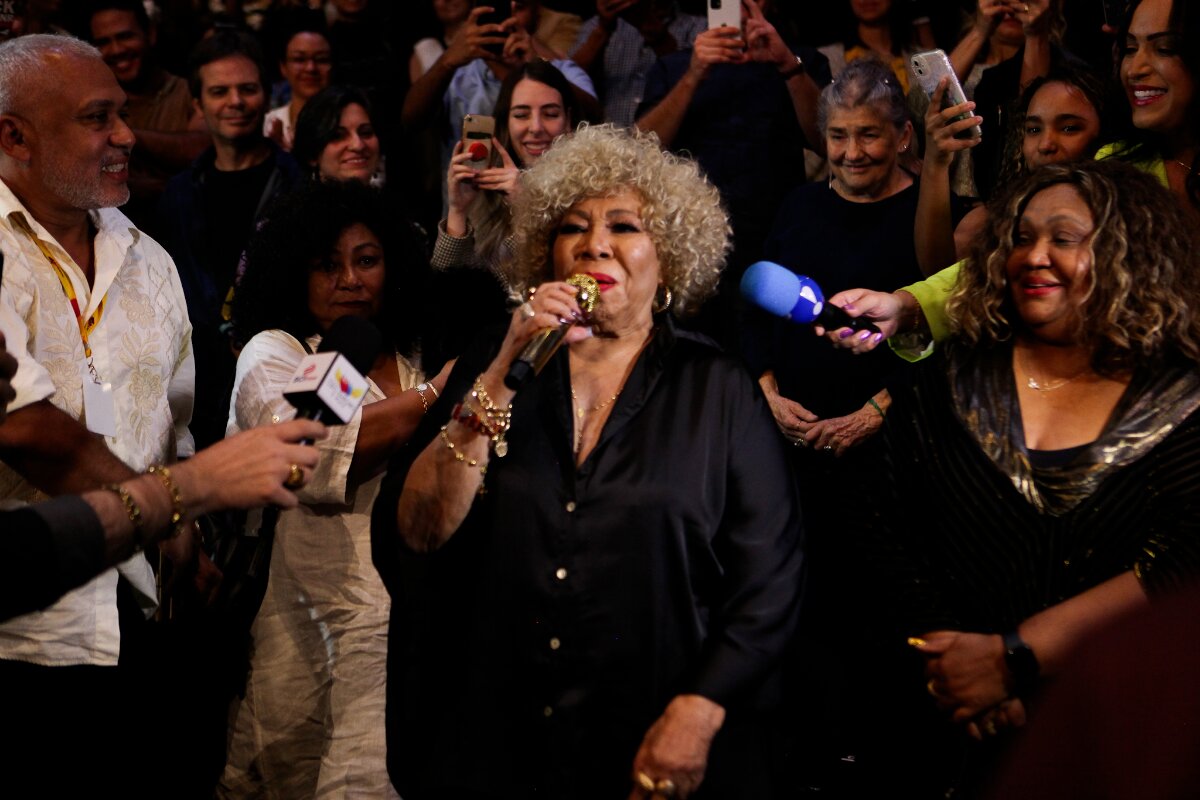 Alcione de roupa preta, falando ao microfone na plateia do teatro