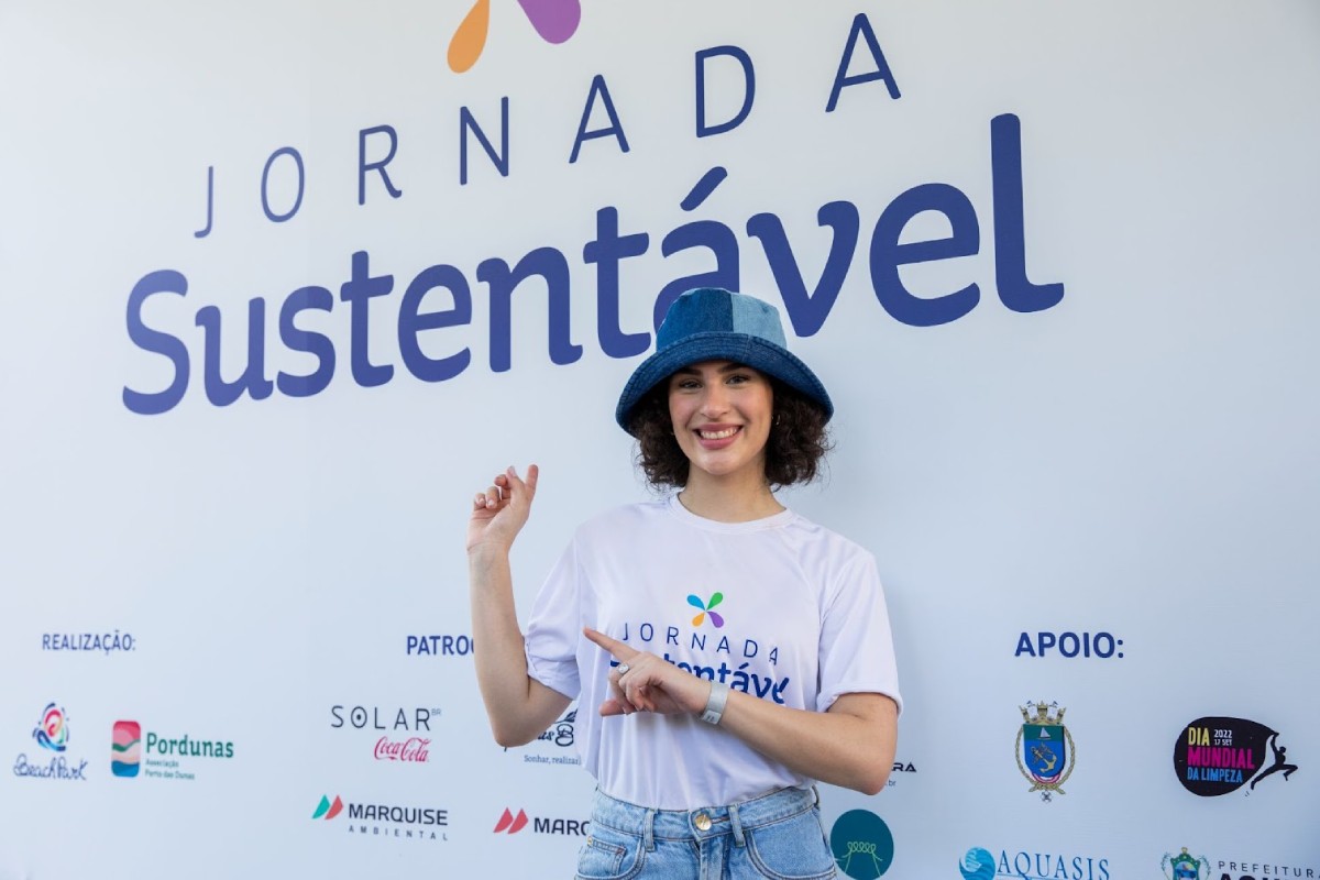 Lívian Aragão posando em frente a painel de jornada sustentável