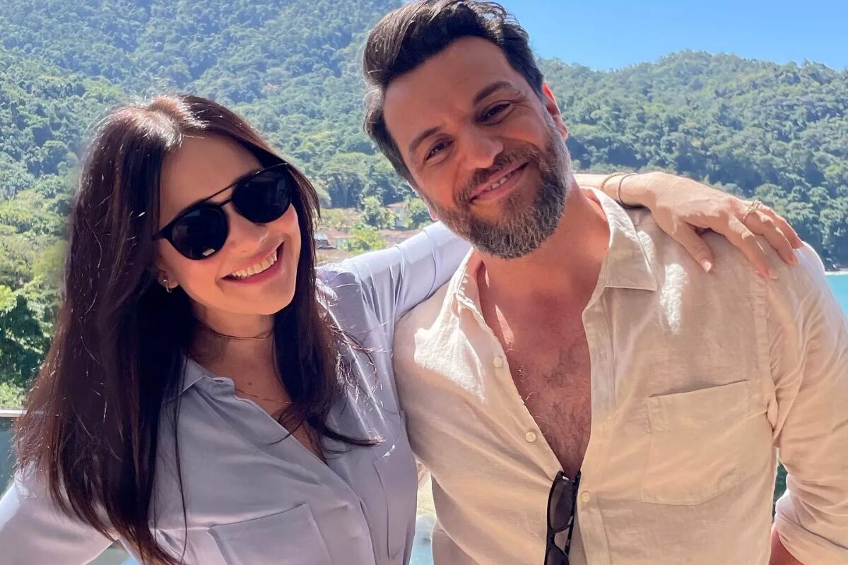 Alessandra Negrini e camisa social branca e óculos escuros abraçada a Rodrigo Lombardi, que está de camisa social bege, ambos sorrindo