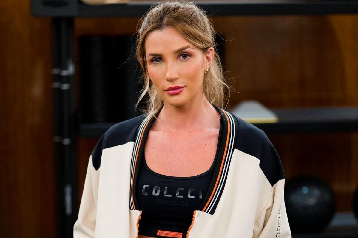 Aline Gotschalg de cabelo preso, expressão séria, de casaco branco e preto com cropped preto