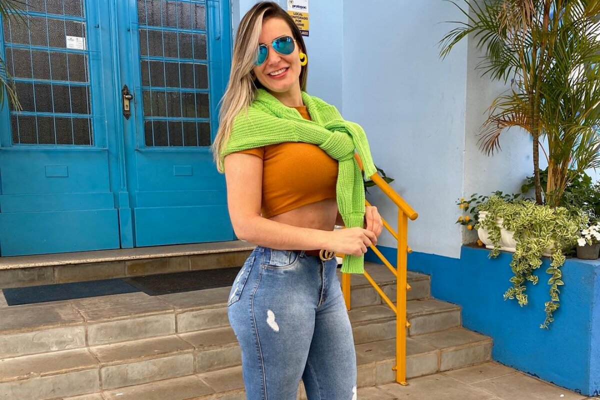 Andressa Urach de calça jeans, cropped marrom, casaco verde nas costas e óculos escuros