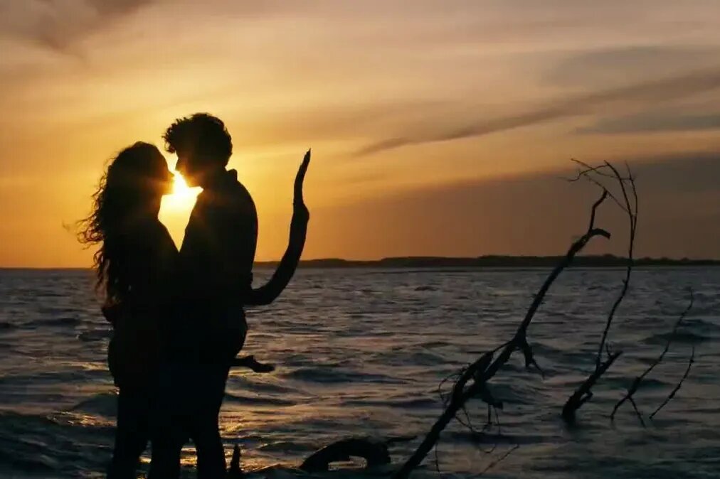 Brisa (Lucy Alves) e Ari (Chay Suede) sob o por do sol em uma praia, na penumbra