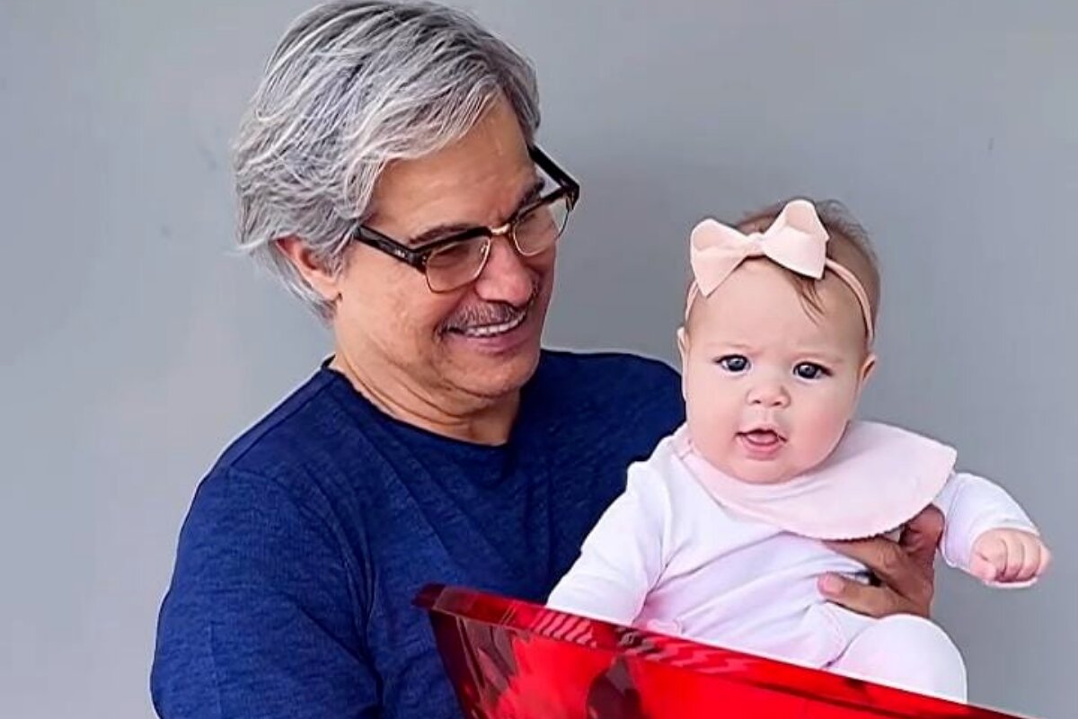 Edson Celulari de camisa azul escura segurando a filha, Chiara, de roupinha rosa clara, dentro de um pote vermelho