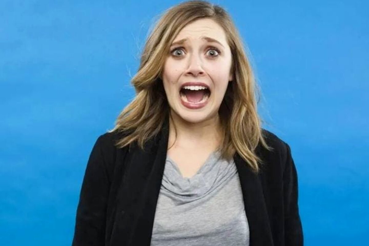 Elizabeth Olsen de boca aberta, expressão de desespero, blazer preto e camisa cinza