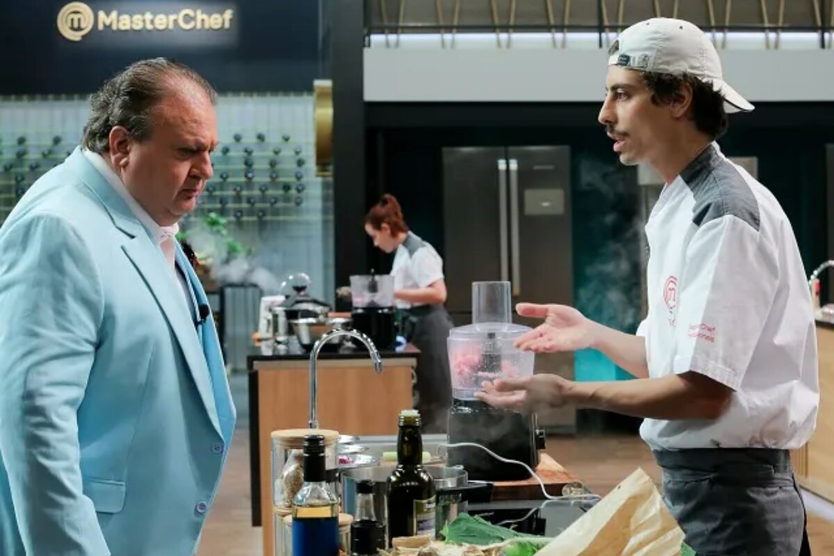 Eric Jacquin na bancada do Masterchef diante do participante Enzo, que apresenta uma iguaria