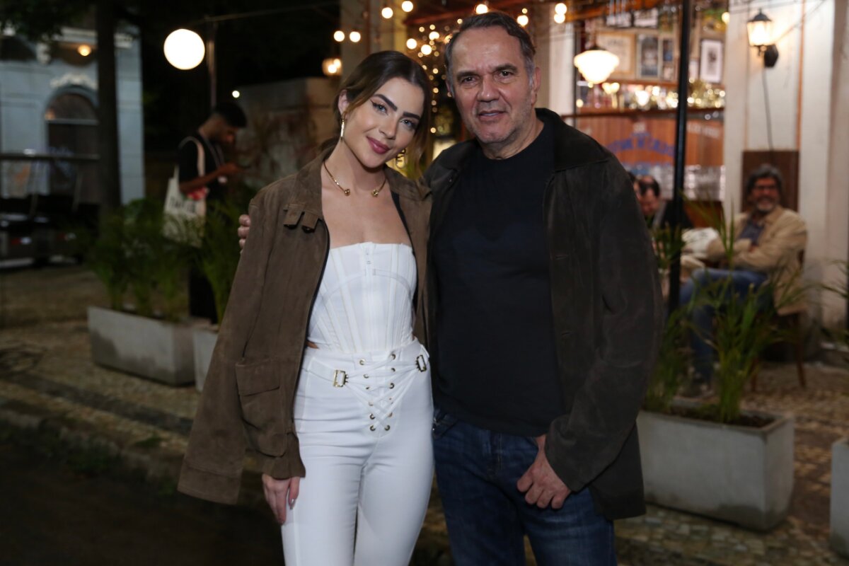 Jade Picon de calça branca, body branco tomara que caia e jaqueta marrom, abraçada a Humberto Martins, que veste calça jeans, camisa preta e jaqueta