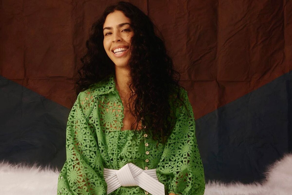 Bela Gil de vestido verde com faixa branca na cintura, sorrindo, de cabelos soltos