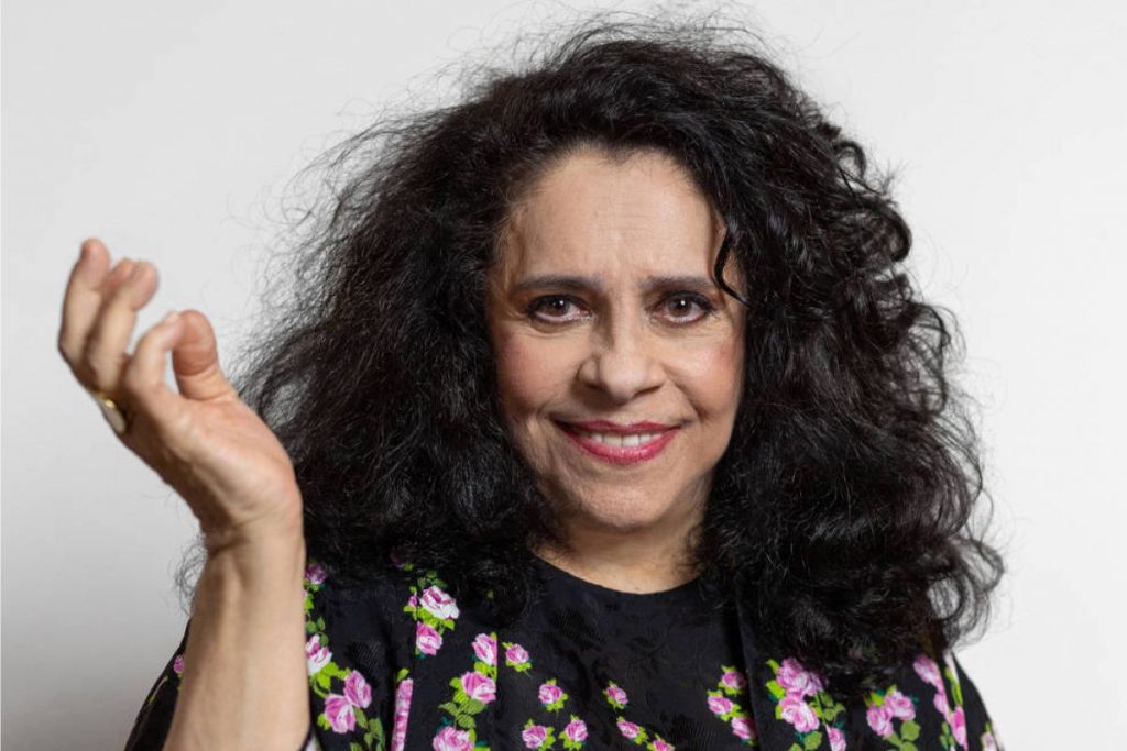 Gal Costa com a mão levantada, sorrindo