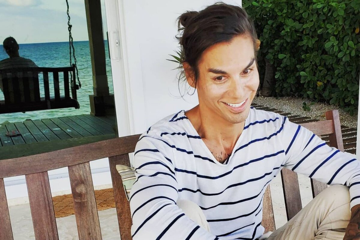 Julio Iglesias Jr. de camisa branca de listras pretas, cabelo preso, sorrindo, sentado