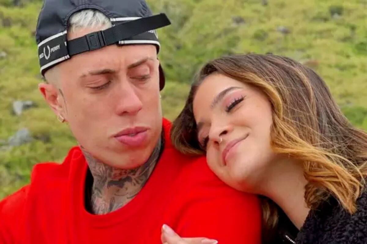 MC Daniel de camisa vermelha e boné preto virado pra trás, olhando para Mel Maia , que está om a cabeça deitada no ombro dele, de olhos fechados