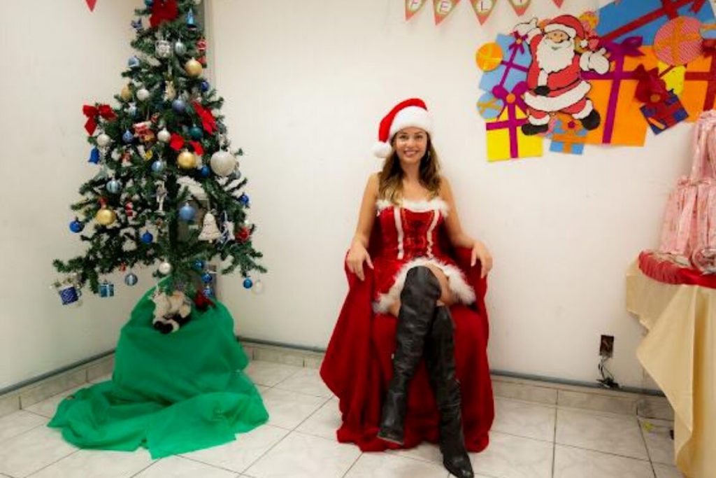 Maria Melilo vestida de Mamãe Noel, sentada ao ado da árvore de Natal