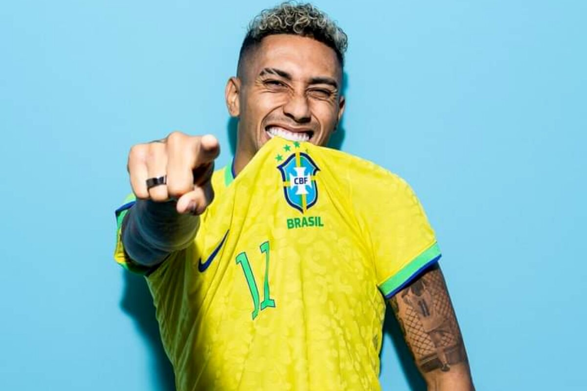 Raphinha mordendo a camisa da seleção e apontando pra frente