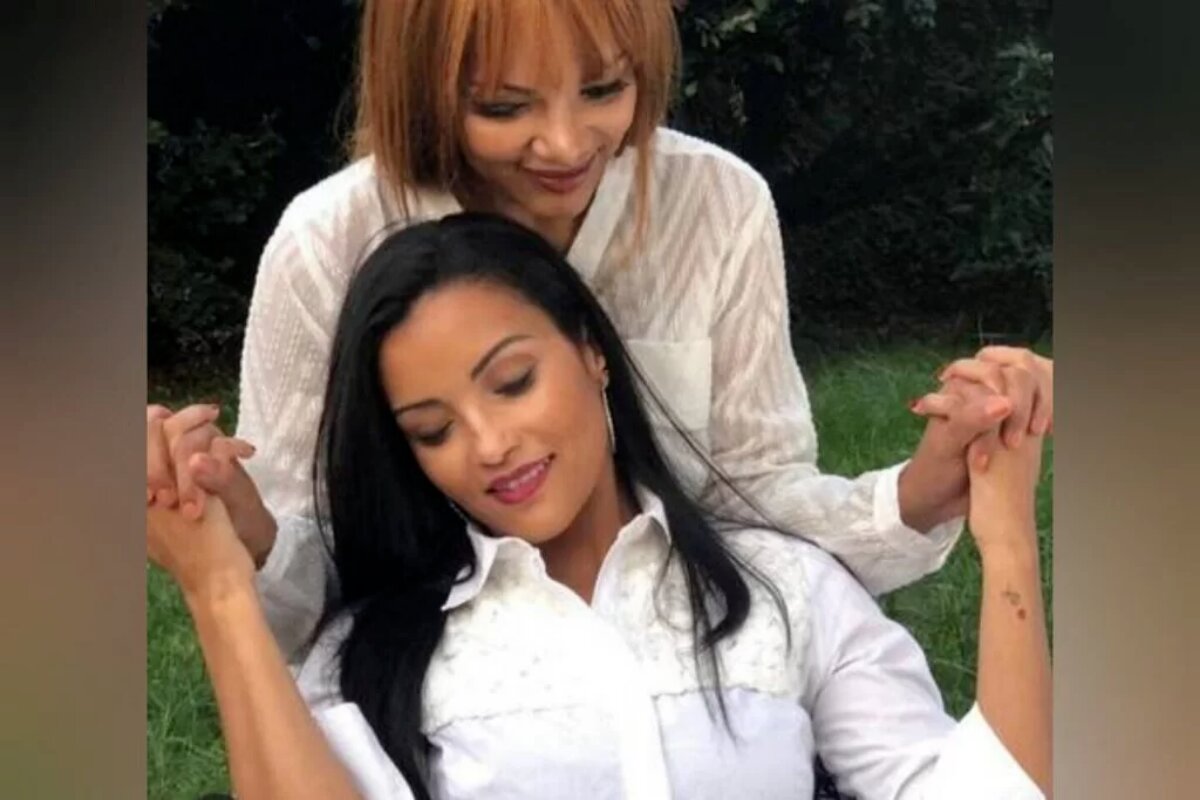 Flordelis em pé, de mão dadas com a filha Simone, que está sentada, ambas de branco