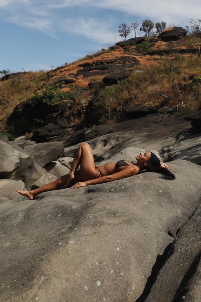 Bella Campos deitada na pedra de biquíni preto