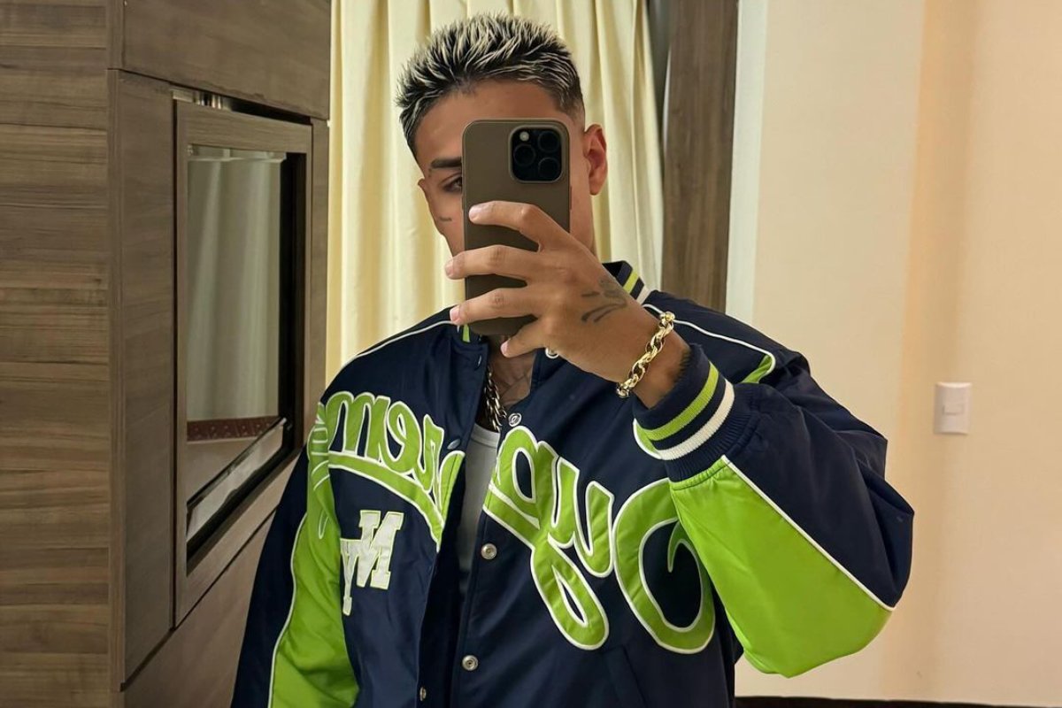 mc cabelinho tirando selfie com casaco azul e verde