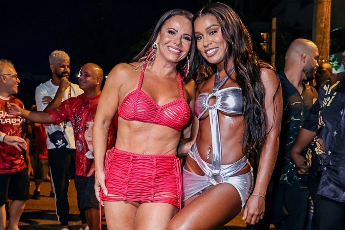 Viviane Araújo de short e top vermelho abraçada a MC Rebecca, de saia e top prata de recortes