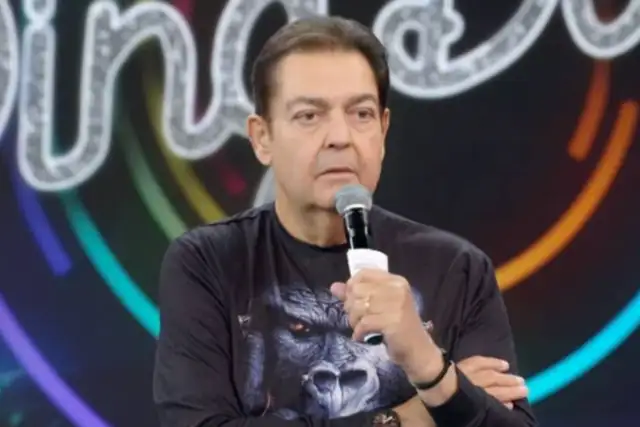 Fausto Silva, no palco de programa de TV, segurando microfone